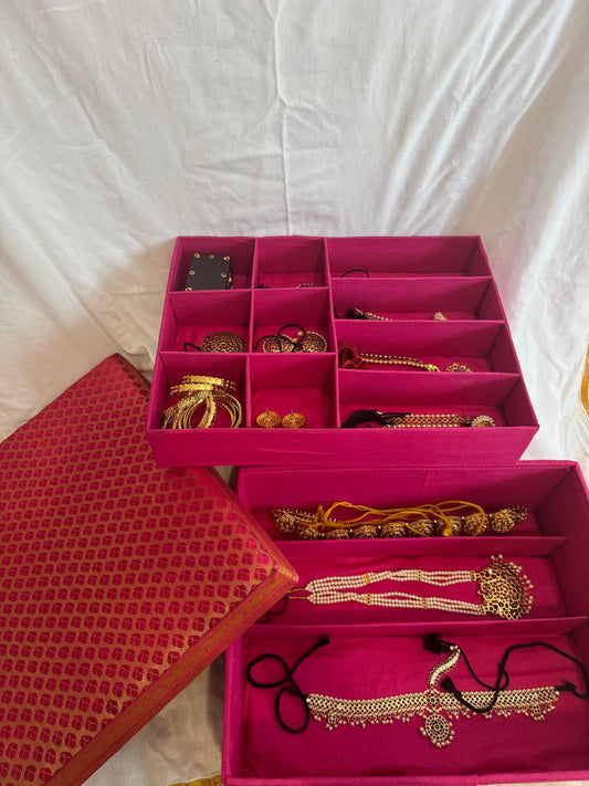 Pink jewelry box with gold necklaces and bangles on a white fabric background