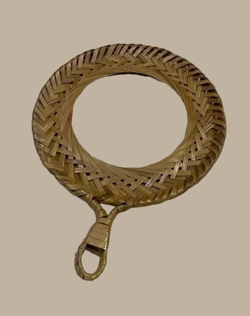 A round hand mirror with a woven natural bamboo or rattan frame and a hanging loop handle, shown on a plain off-white surface.